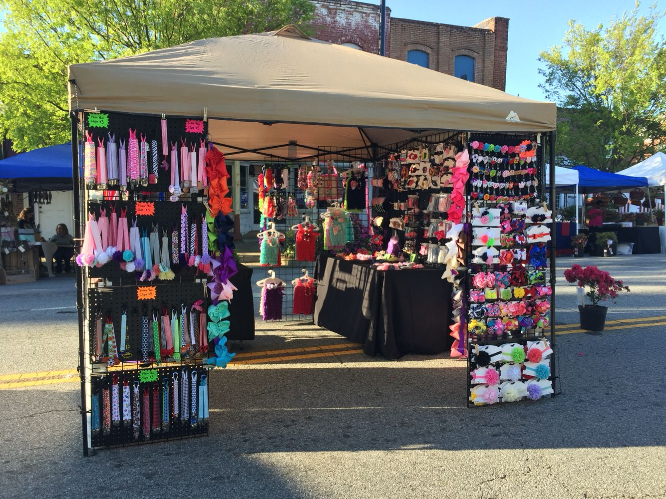 Outdoor market stall with colorful knitted products under a beige canopy.