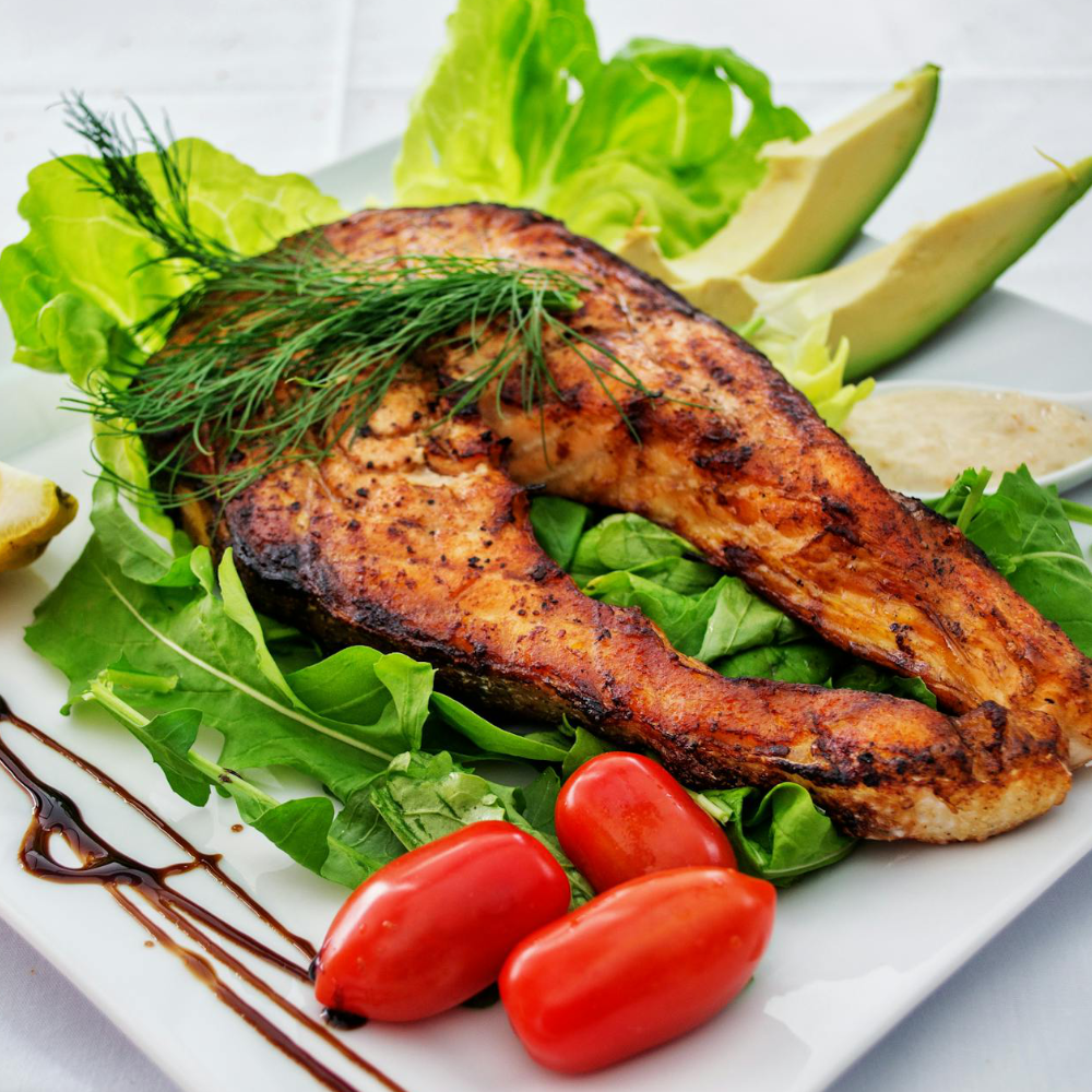 Grilled salmon fillet on a bed of greens with tomatoes and avocado slices.