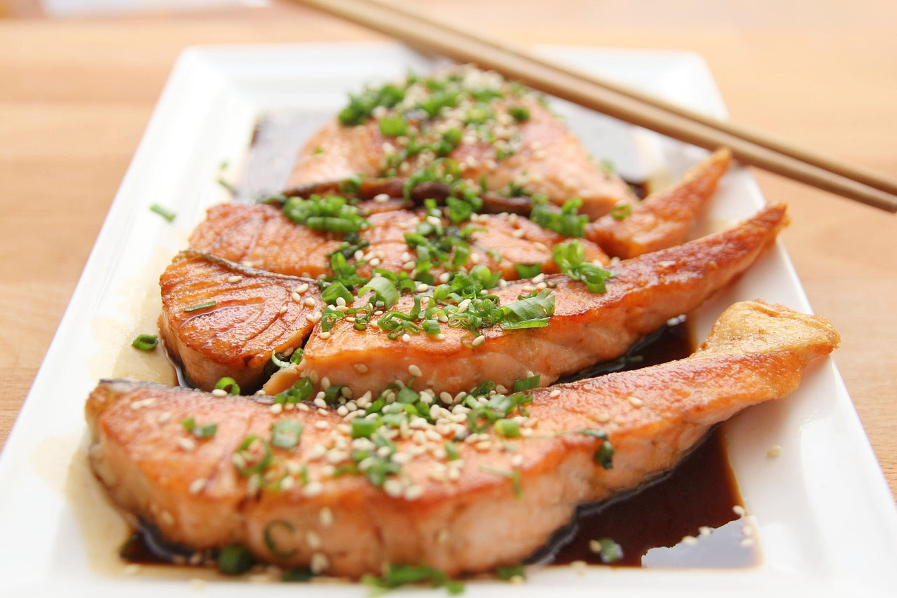 Salmon dish with green onions on a white plate with chopsticks