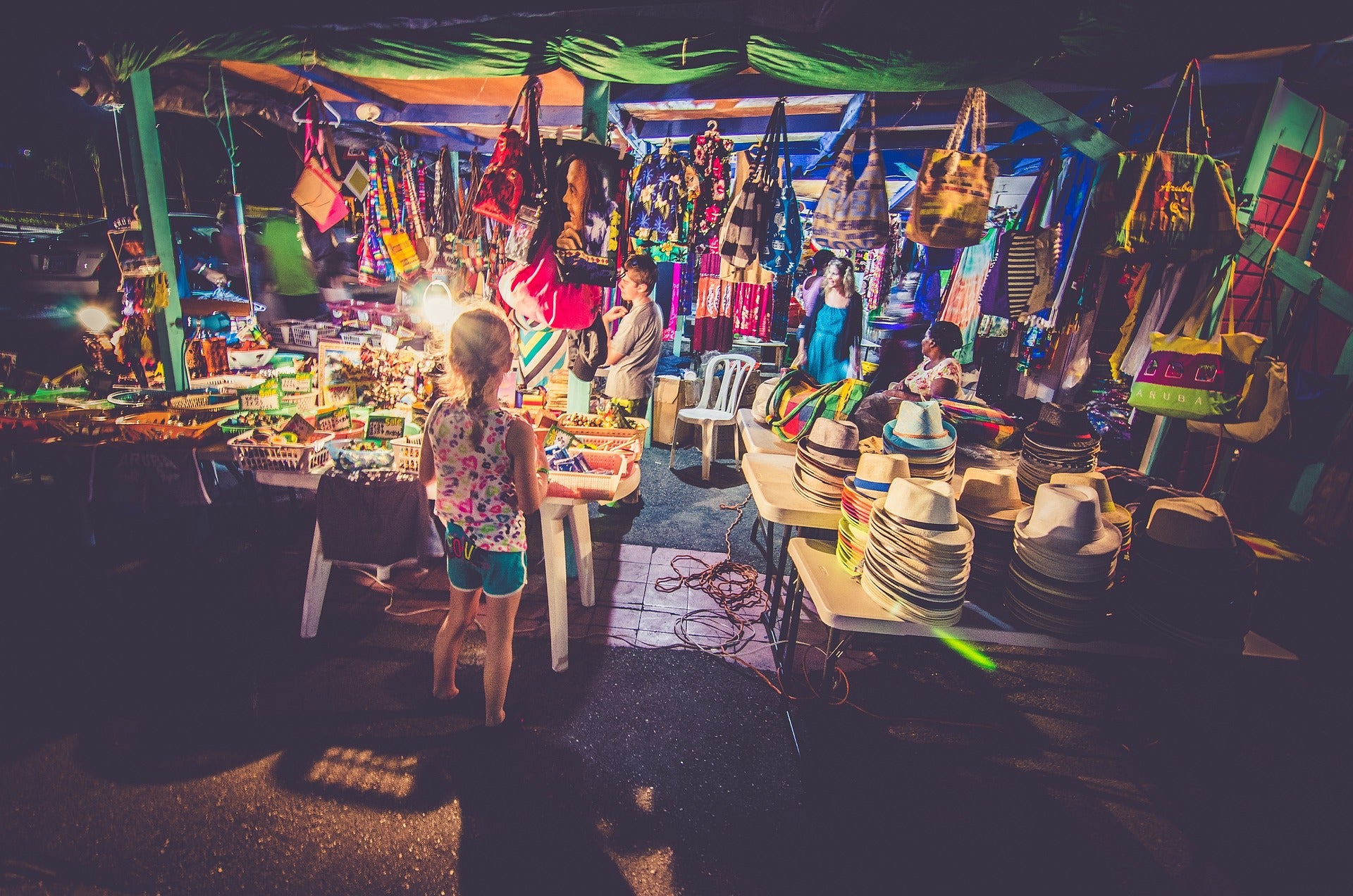 Nighttime outdoor market with stalls and a child standing near a table.