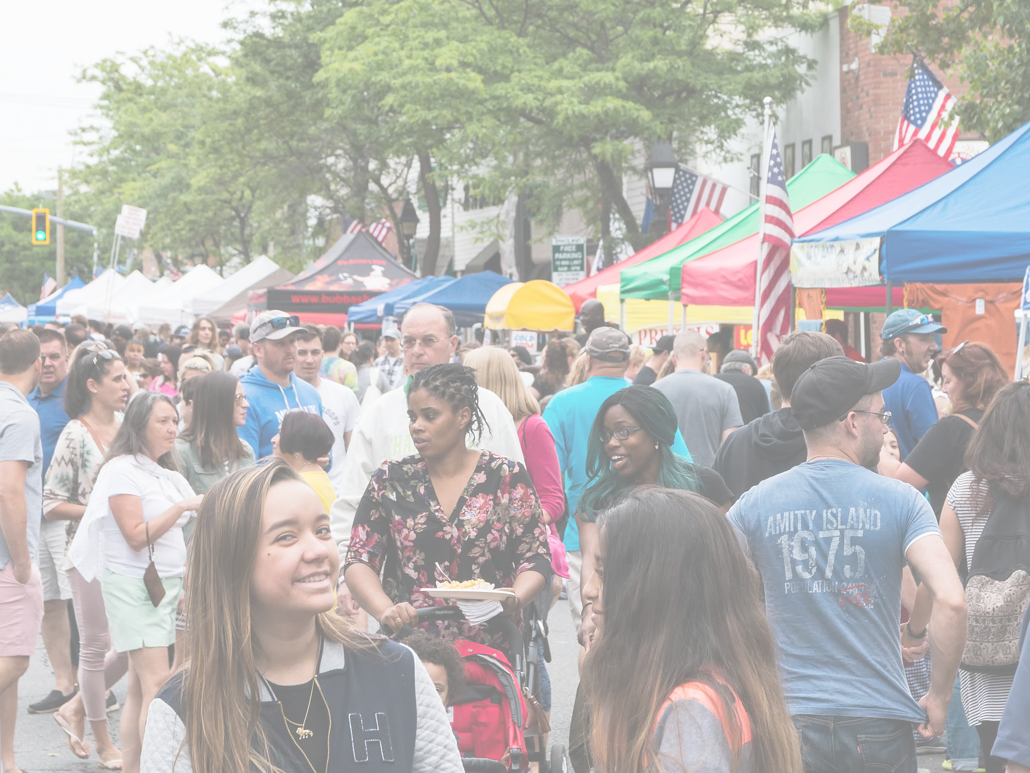 Crowded outdoor market with people and colorful tents under a clear sky.
